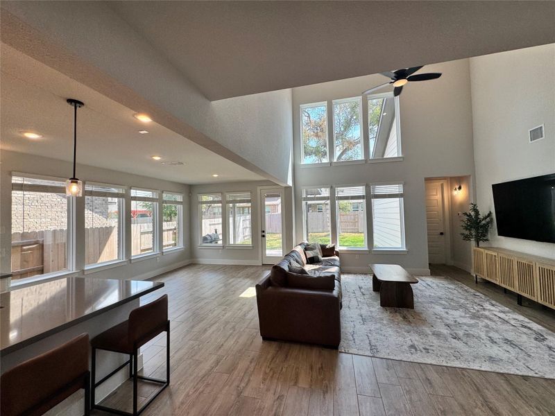 Living room featuring light wood finished floors, plenty of natural light, a towering ceiling, a ceiling fan, and recessed lighting