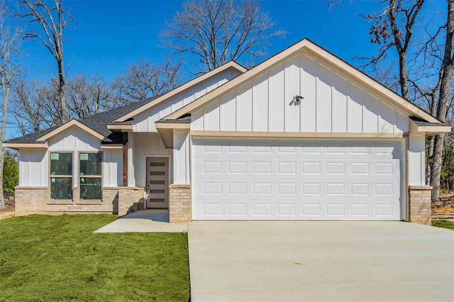 View of front of property with an attached garage, brick siding, a shingled roof, driveway, and board and batten siding