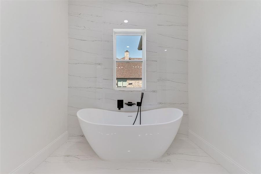 Freestanding soaking tub with matte black fixtures, set against a tiled accent wall featuring a vertical window Freestanding soaking tub with matte black fixtures, set against a tiled accent wall featuring a vertical window