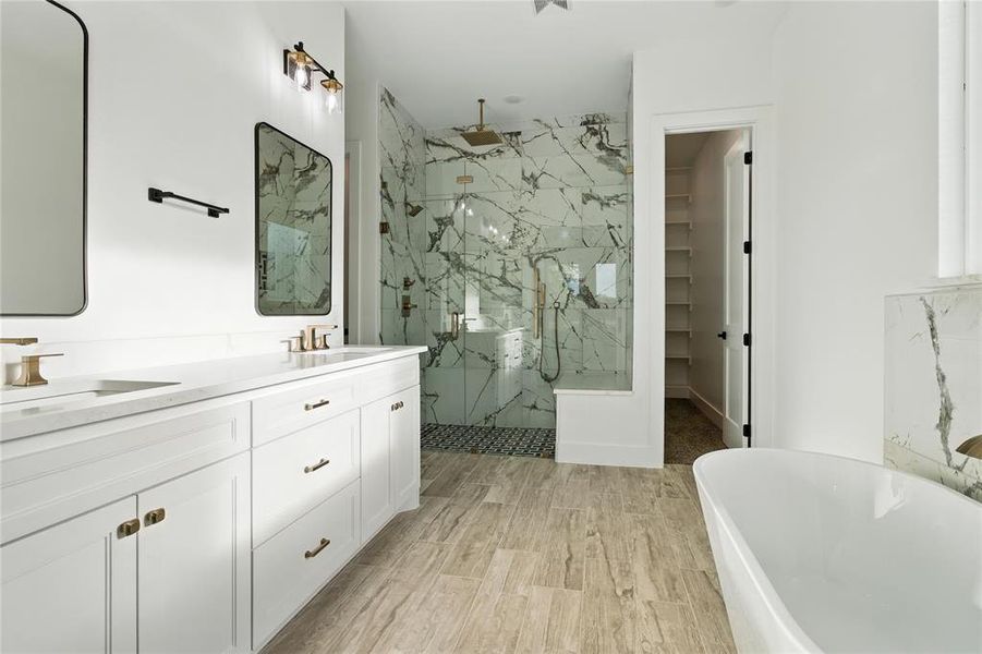 Full bathroom featuring a marble finish shower, a soaking tub, double vanity, wood finished floors, and a spacious closet Full bathroom featuring a marble finish shower, a soaking tub, double vanity, wood finished floors, and a spacious closet