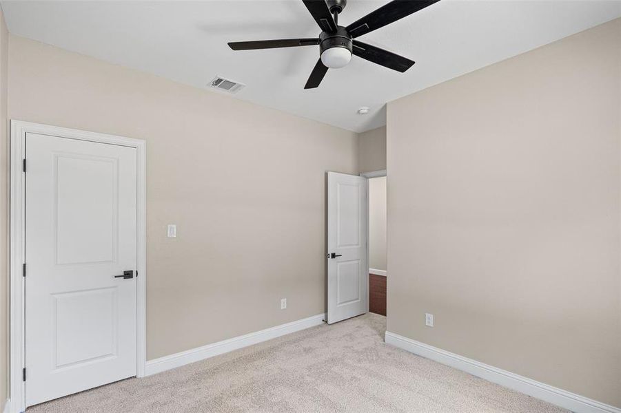 Carpeted room featuring a ceiling fan with integrated lighting, a paneled door with matte black hardware, and a second interior door