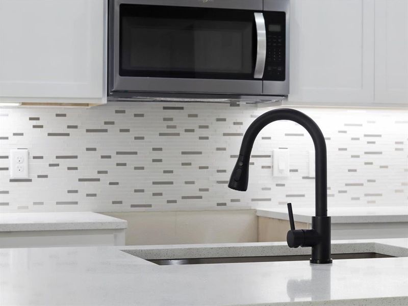 Kitchen view of stainless steel microwave, decorative backsplash, light stone countertops, and white cabinets Kitchen view of stainless steel microwave, decorative backsplash, light stone countertops, and white cabinets