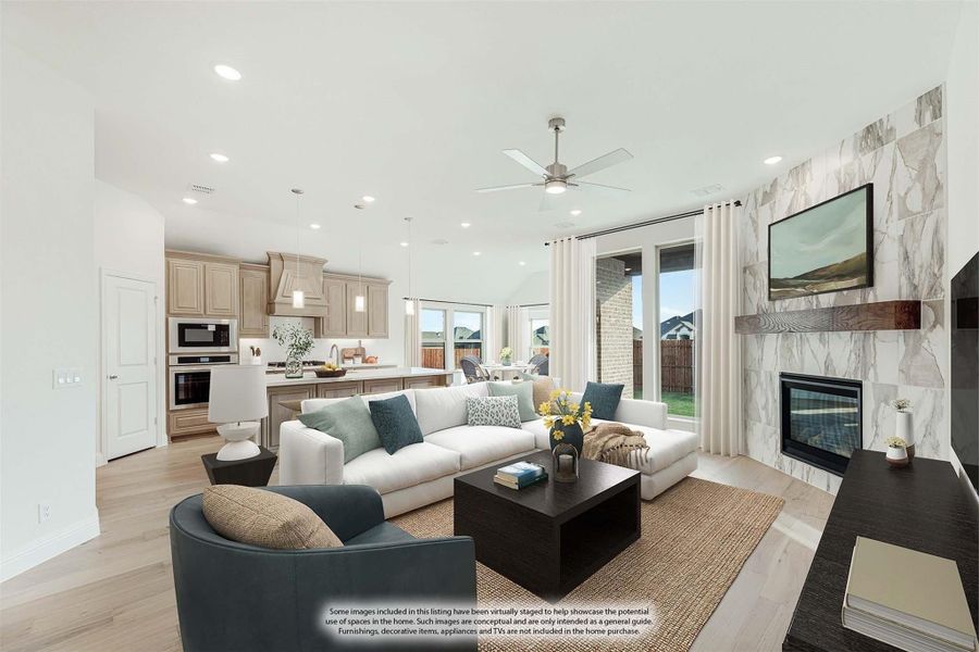Open-concept living room with marble fireplace, ceiling fan, and kitchen visible in background