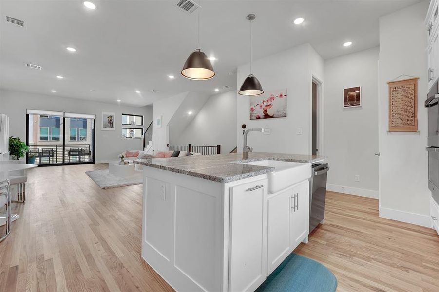 Kitchen with white cabinets, sink, light wood-type flooring, an island with sink, and decorative light fixtures