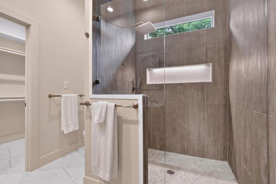 Glass-enclosed shower with a rainfall showerhead, integrated niche, and patterned floor tile