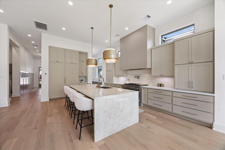 At the heart of the home, the chef’s kitchen is outfitted with a Fisher & Paykel appliance package, including a 48” six-burner range with griddle and double ovens, a pot filler, walk-in pantry, and a large waterfall-edge island.