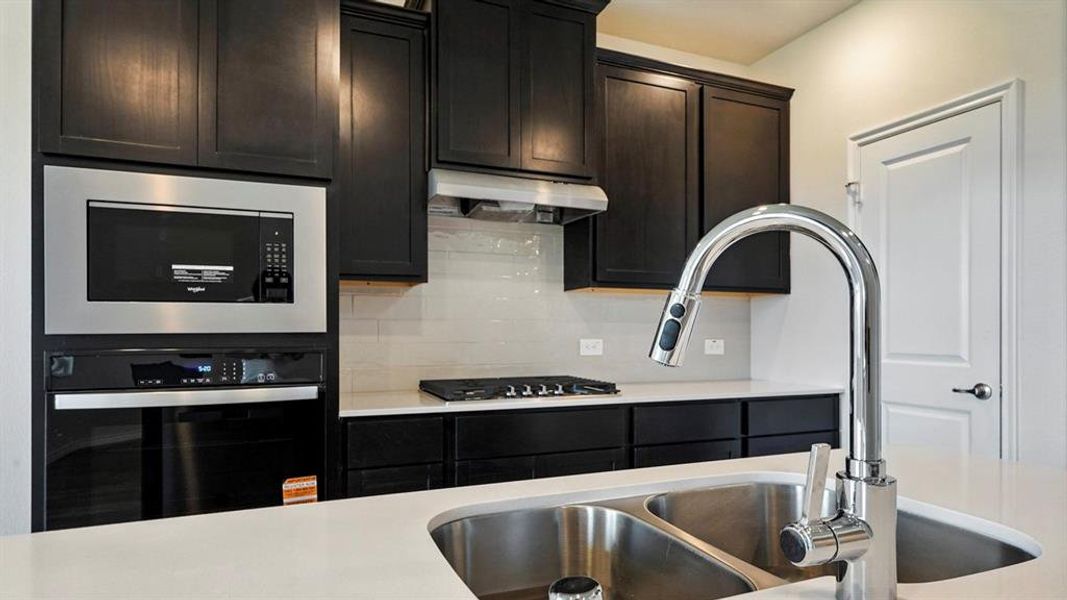 Kitchen featuring black appliances, tasteful backsplash, light stone counters, and dark cabinetry
