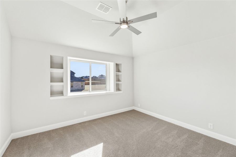 Empty bedroom with vaulted ceiling, ceiling fan, built-in shelves, and carpet flooring Empty bedroom with vaulted ceiling, ceiling fan, built-in shelves, and carpet flooring