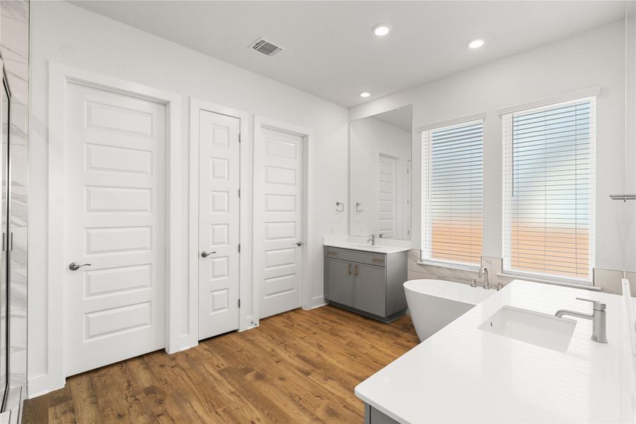A well-lit bathroom features dual vanities, a freestanding tub, and rich wood-toned flooring. A well-lit bathroom features dual vanities, a freestanding tub, and rich wood-toned flooring.