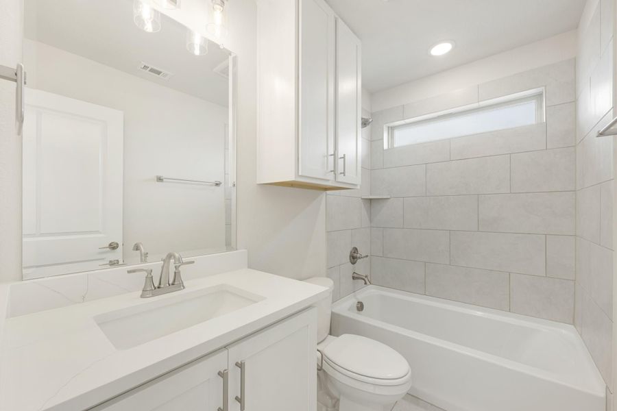 Bathroom with white vanity, quartz countertop, soaking tub, and gray tile surround