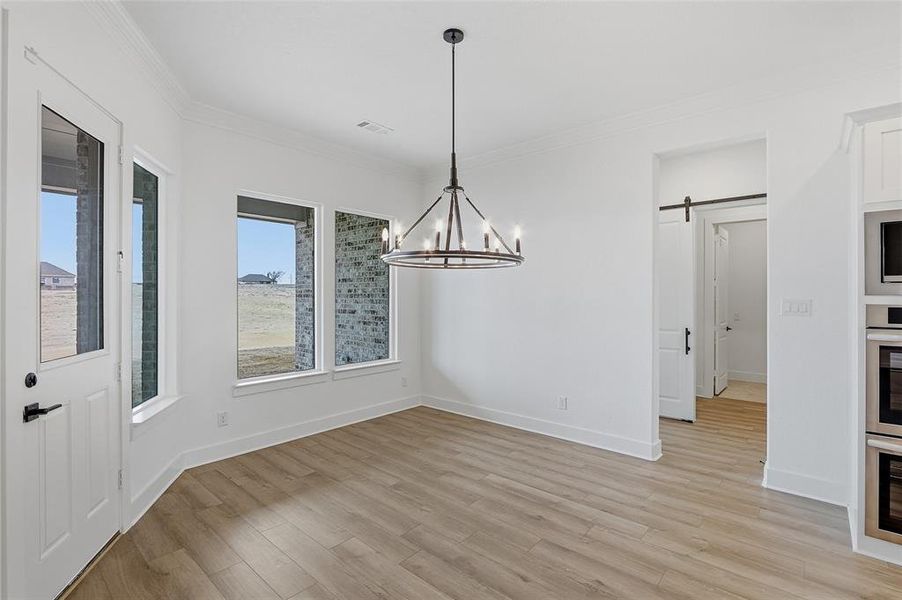 Unfurnished dining area featuring a barn door, ornamental molding, light wood-style floors, and hanging lights