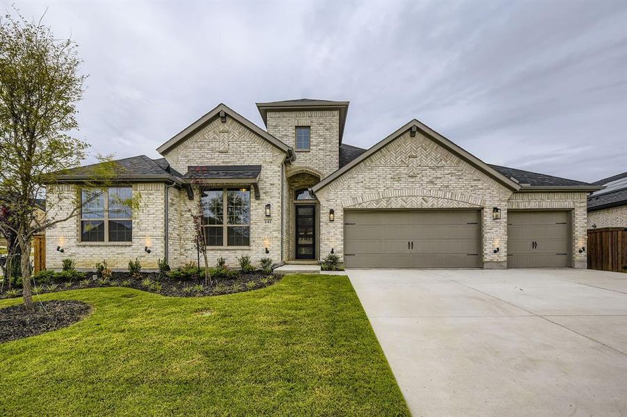 French country home with an attached garage, concrete driveway, a front lawn, brick siding, and roof with shingles French country home with an attached garage, concrete driveway, a front lawn, brick siding, and roof with shingles