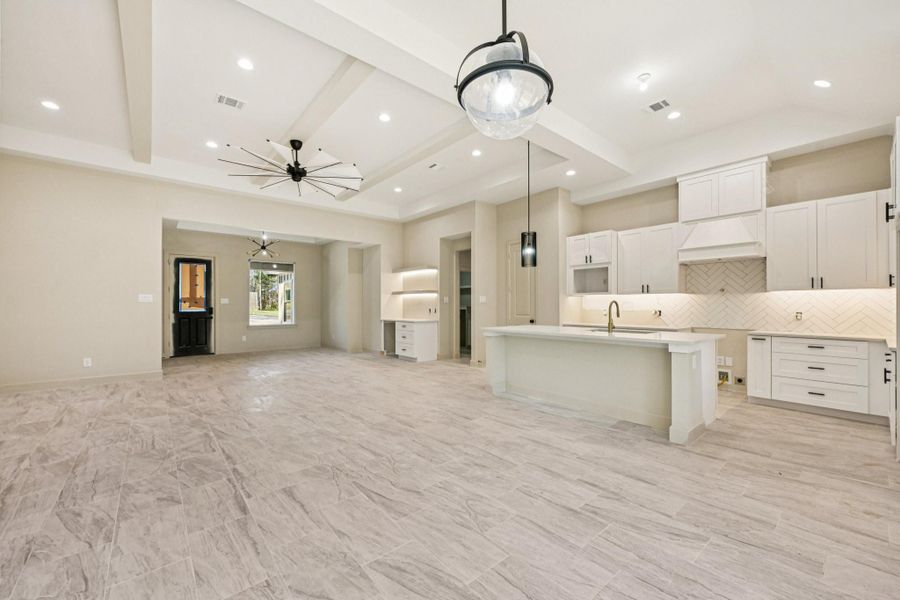 Spacious open-concept living area features a modern kitchen with a large island, elegant white cabinetry, and contemporary pendant lighting.
