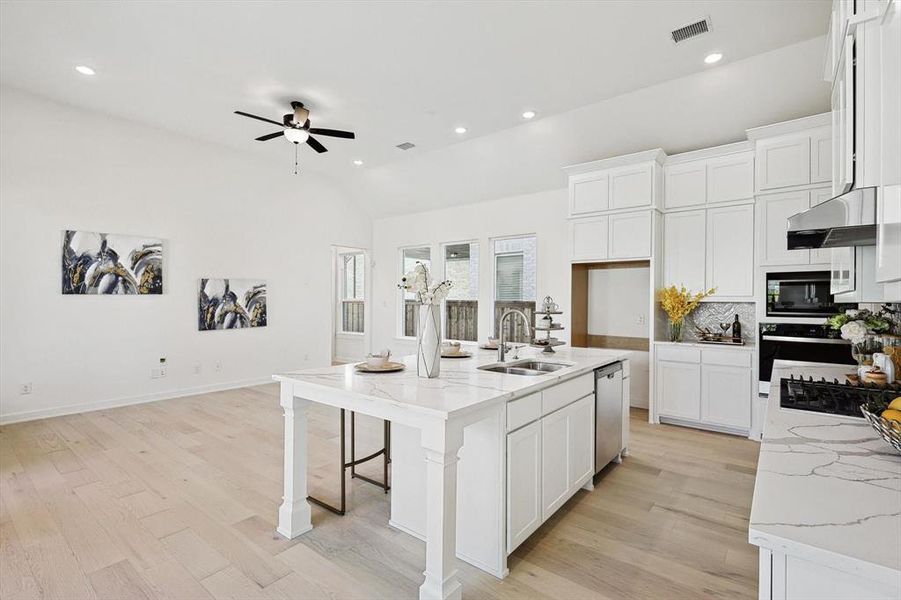 Kitchen with ceiling fan, sink, a center island with sink, dishwasher, and light stone countertops