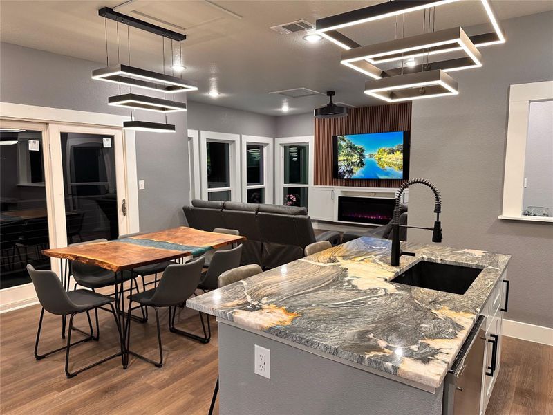 Modern design featuring a center island with sink, a fireplace, exquisite countertops, wood-grain flooring, and accoustic wall accents Modern design featuring a center island with sink, a fireplace, exquisite countertops, wood-grain flooring, and accoustic wall accents
