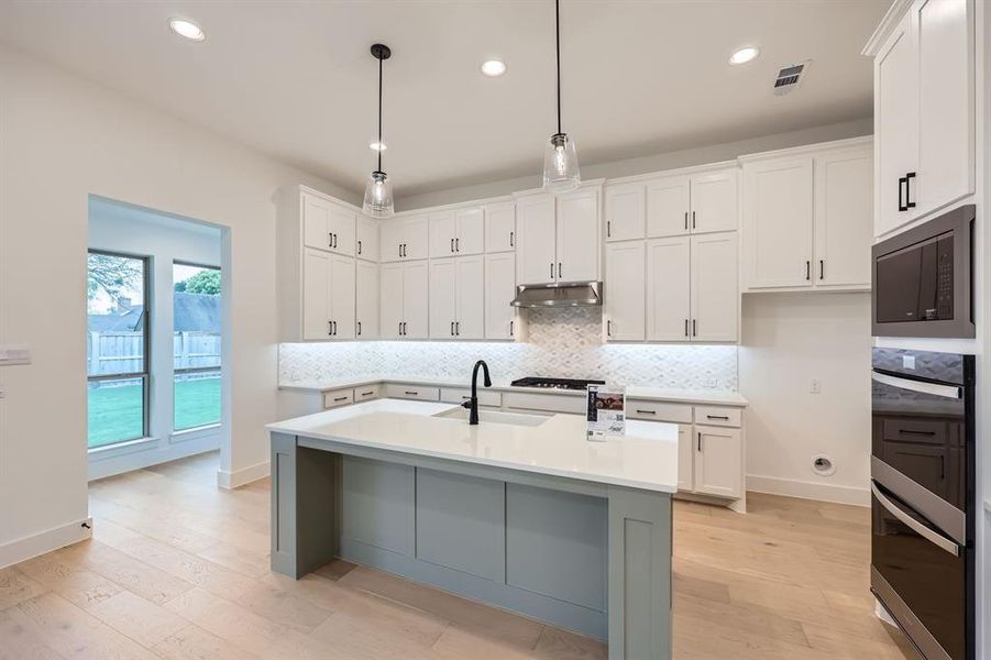 Kitchen with white cabinets, black microwave, sink, and an island with sink