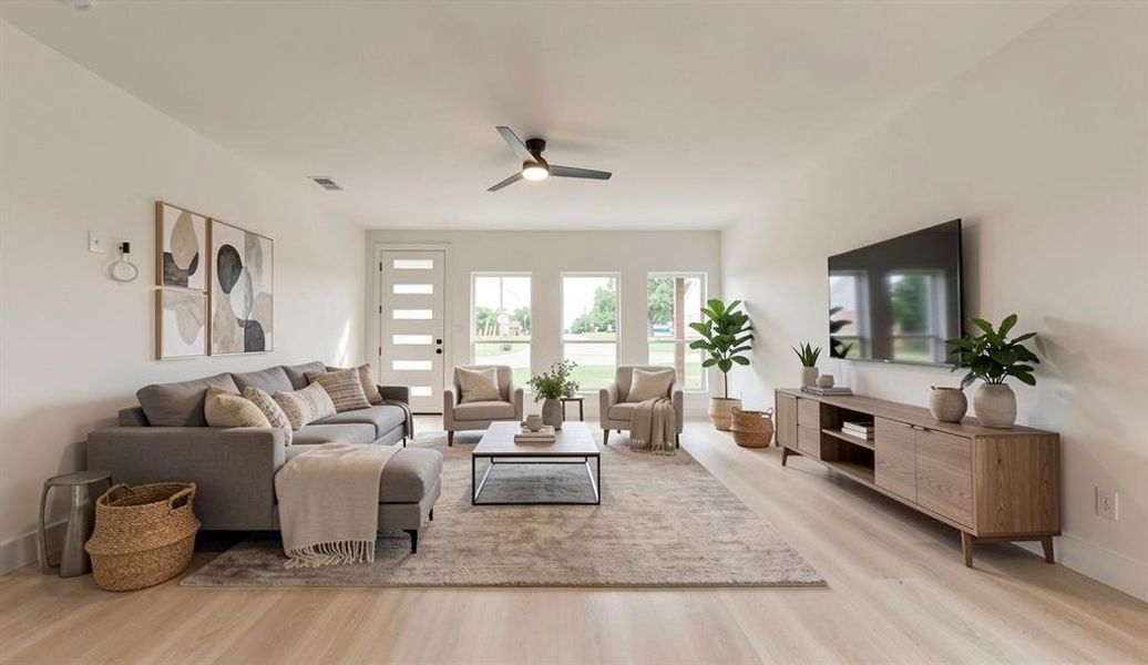 Spacious room featuring light wood-finish flooring, a modern ceiling fan, multiple windows providing natural light, and a contemporary white door with frosted glass panels
