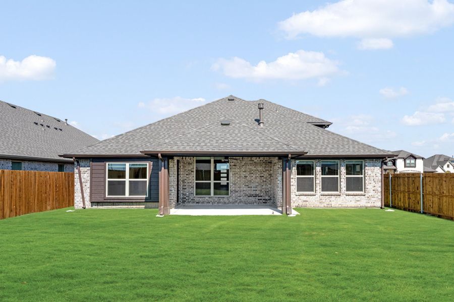 Rear view of single-story brick home with covered patio, large backyard, and wood privacy fence Rear view of single-story brick home with covered patio, large backyard, and wood privacy fence