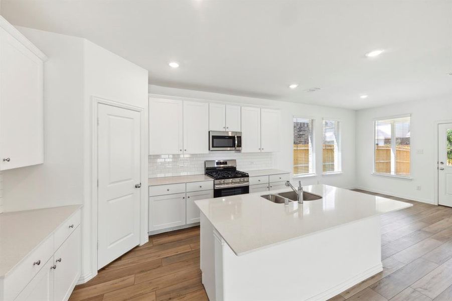 Kitchen with a kitchen island with sink, backsplash, sink, appliances with stainless steel finishes, and white cabinets