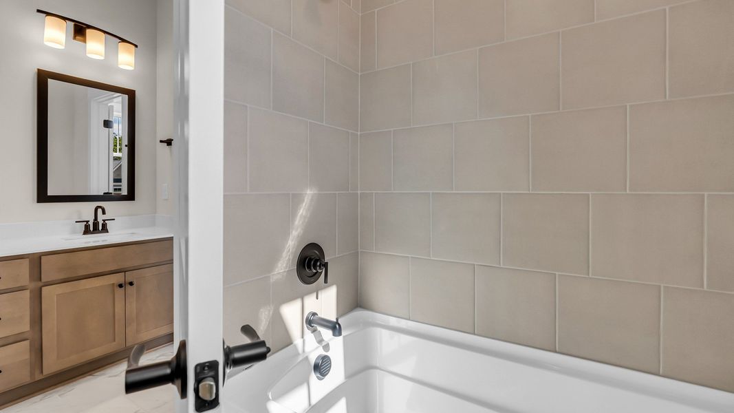 Secondary bathroom with tiled shower and dual sink vanity (Representative of finished home)