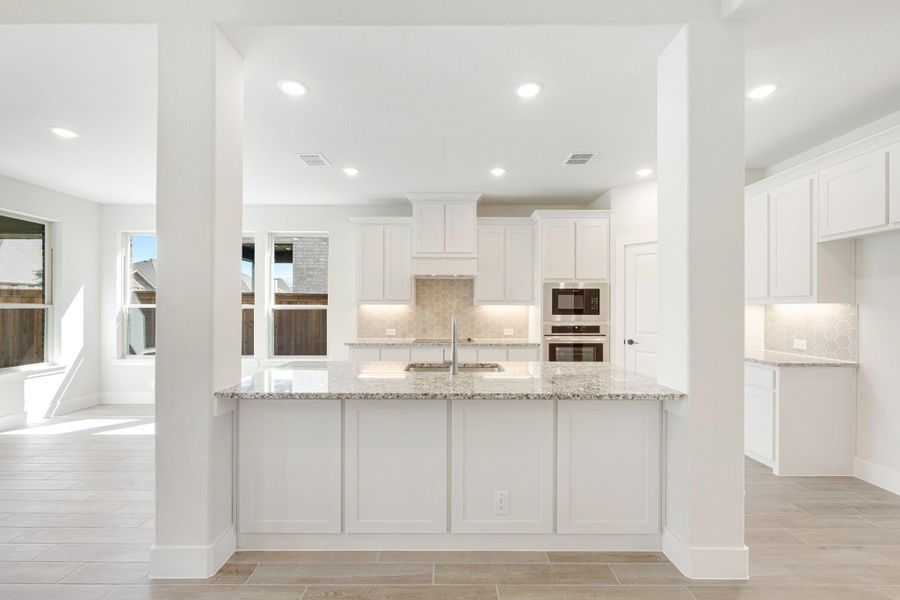 Kitchen with large granite island, white cabinets, tile backsplash, and built-in stainless steel appliances