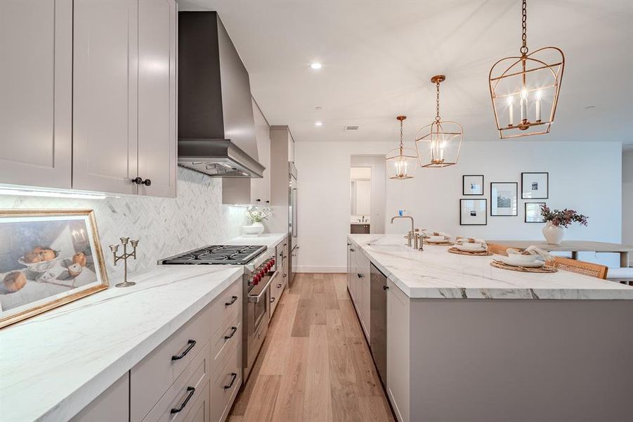 Kitchen with light wood-style flooring, decorative light fixtures, tasteful backsplash, premium appliances, and light stone countertops Kitchen with light wood-style flooring, decorative light fixtures, tasteful backsplash, premium appliances, and light stone countertops