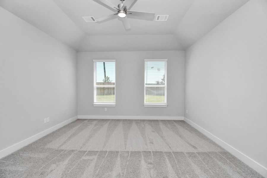 Escape and relax in the exquisite primary suite, a haven to unwind after a long day. The spacious room, located on first floor, boasts plush carpeting, soothing paint tones, high ceilings, and expansive windows adorned with privacy blinds. Sample photo of completed home with similar floor plan. Actual colors and selections may vary.
