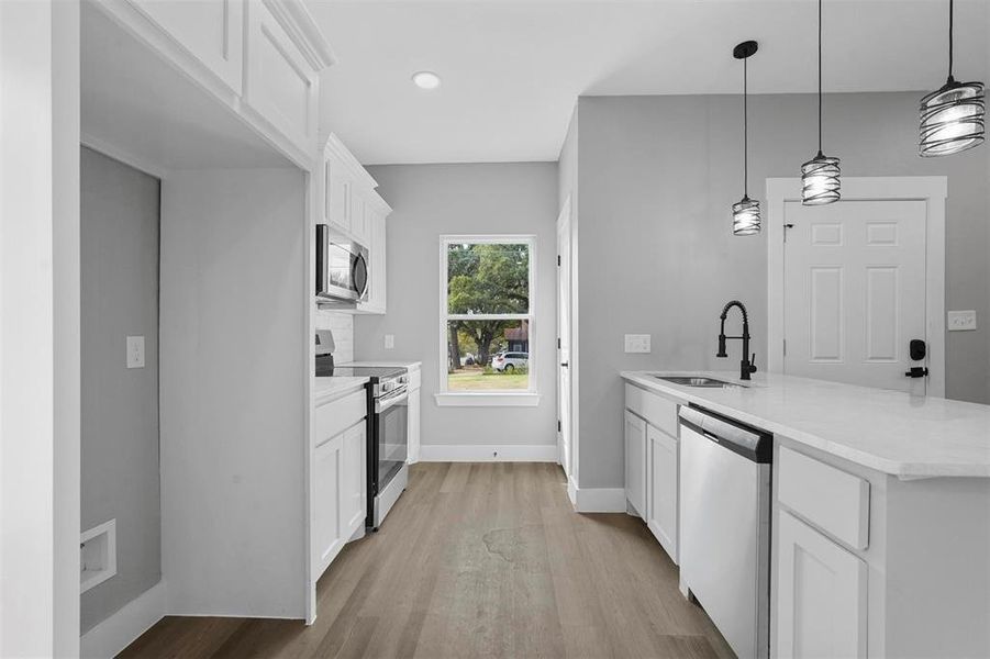 Kitchen with pendant lighting, sink, white cabinetry, stainless steel appliances, and light hardwood / wood-style floors