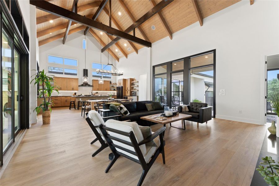 Vaulted wood-paneled ceiling with exposed beams, wood-finish flooring, two sets of expansive glass doors, and a kitchen featuring wood cabinetry and pendant lighting Vaulted wood-paneled ceiling with exposed beams, wood-finish flooring, two sets of expansive glass doors, and a kitchen featuring wood cabinetry and pendant lighting