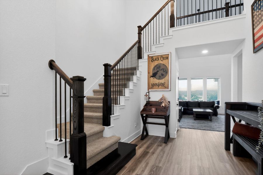 Two-story entry foyer featuring a grand staircase with dark wood newel posts and handrails, black iron balusters, and carpeted treads Two-story entry foyer featuring a grand staircase with dark wood newel posts and handrails, black iron balusters, and carpeted treads