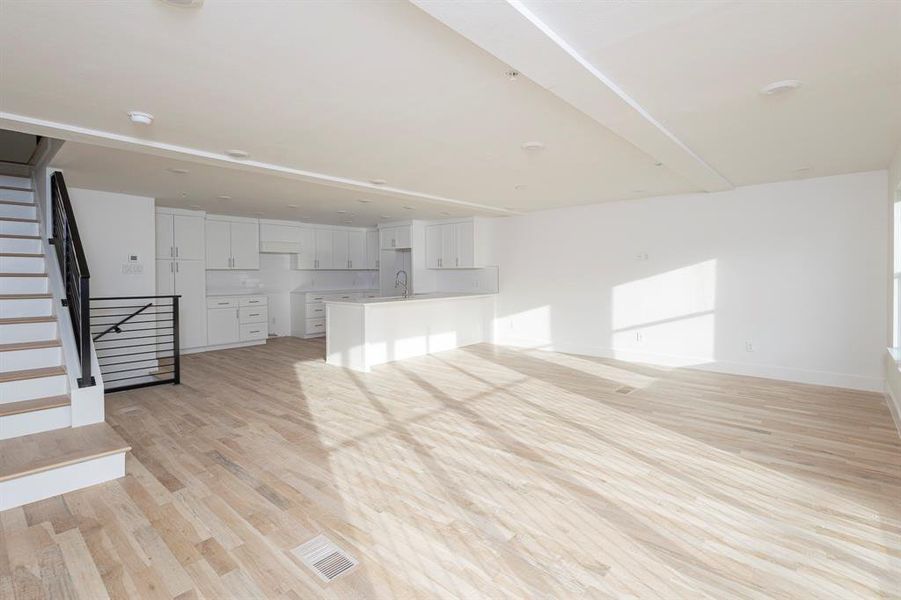 Unfurnished living room with visible vents, stairway, a sink, light wood-type flooring, and baseboards