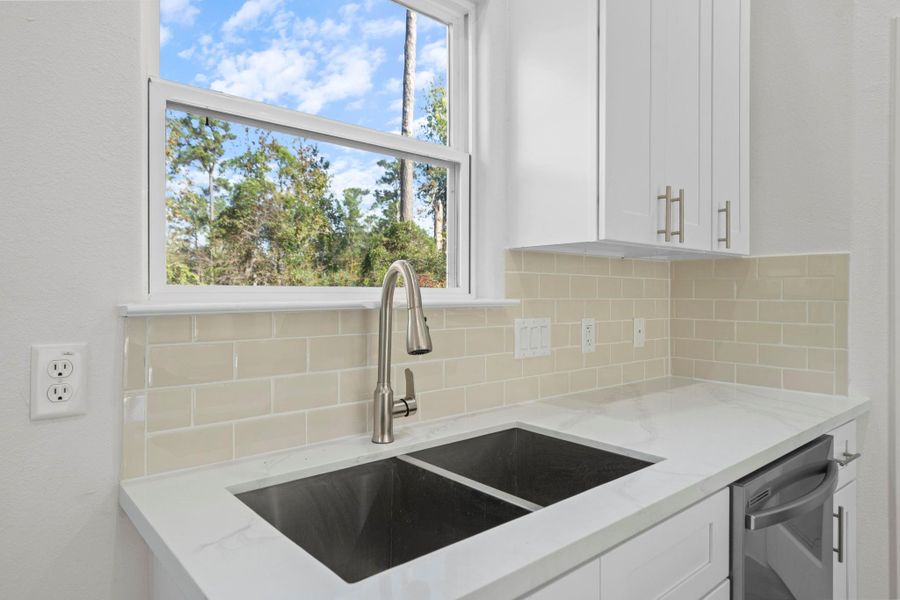 This photo highlights a bright and modern kitchen corner featuring a sleek dual-basin sink with a brushed nickel gooseneck faucet. The white quartz countertops and glossy subway tile backsplash create a clean, polished look.