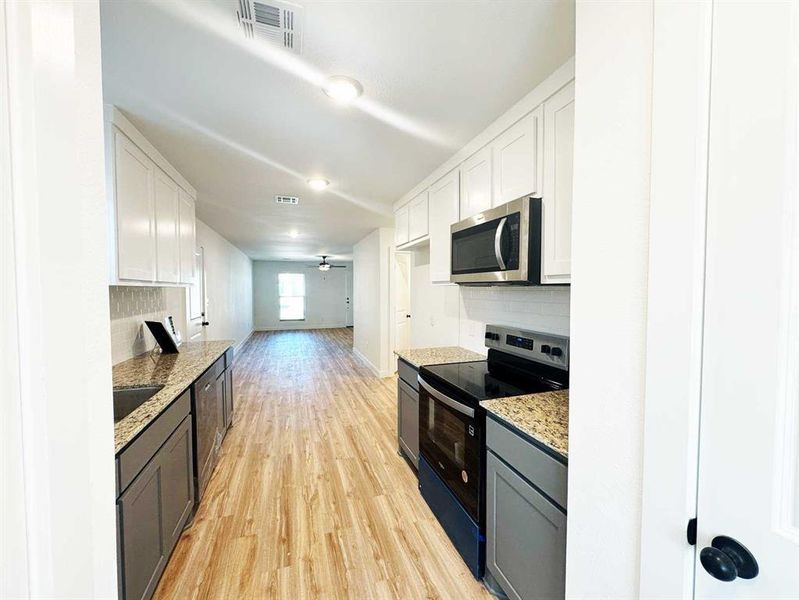 Kitchen featuring decorative backsplash, light wood-style floors, stainless steel appliances, white cabinets, and visible vents