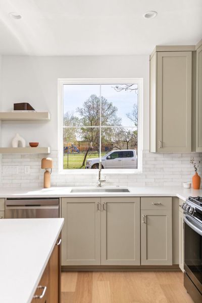 Kitchen featuring stainless steel appliances, open shelves, light wood-type flooring, decorative backsplash, and light stone countertops