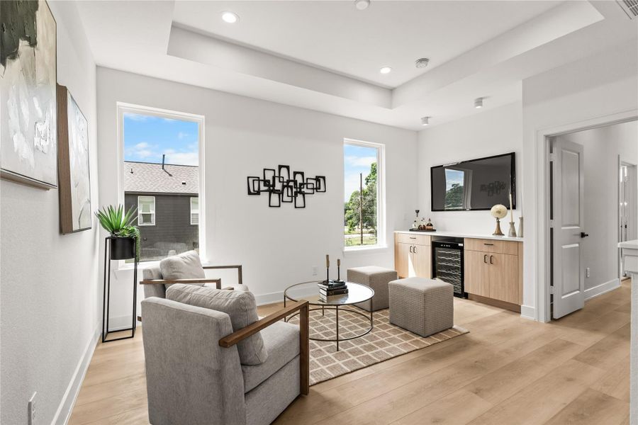 The spacious upstairs flex lounge features elegant tray ceilings and recessed LED lighting. It includes a built-in wet bar with wood cabinets, a white quartz countertop, and a built-in beverage cooler, making it perfect for a second living area, media room, or playroom.
