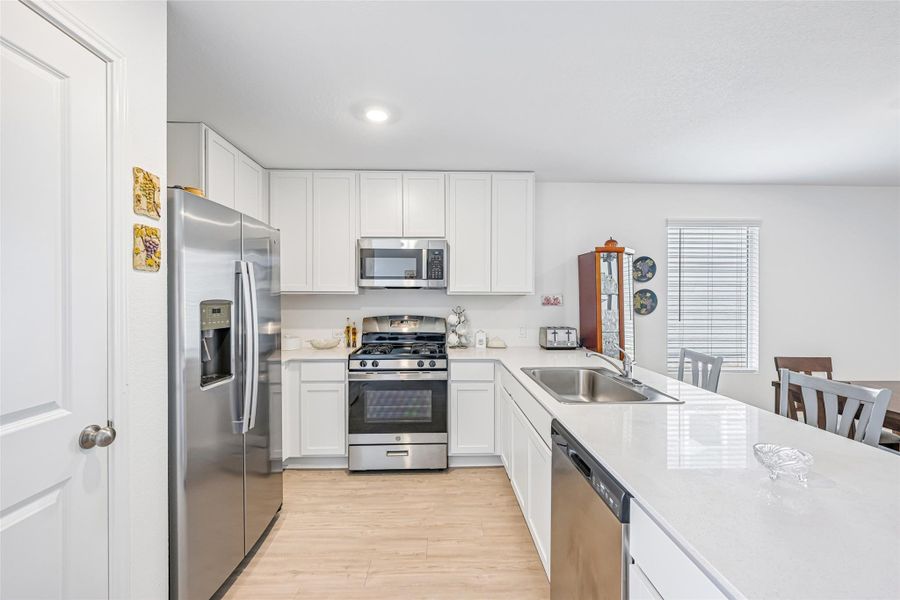 Modern kitchen featuring white cabinetry, stainless steel appliances, light-toned wood-finish flooring, and solid surface countertops Modern kitchen featuring white cabinetry, stainless steel appliances, light-toned wood-finish flooring, and solid surface countertops