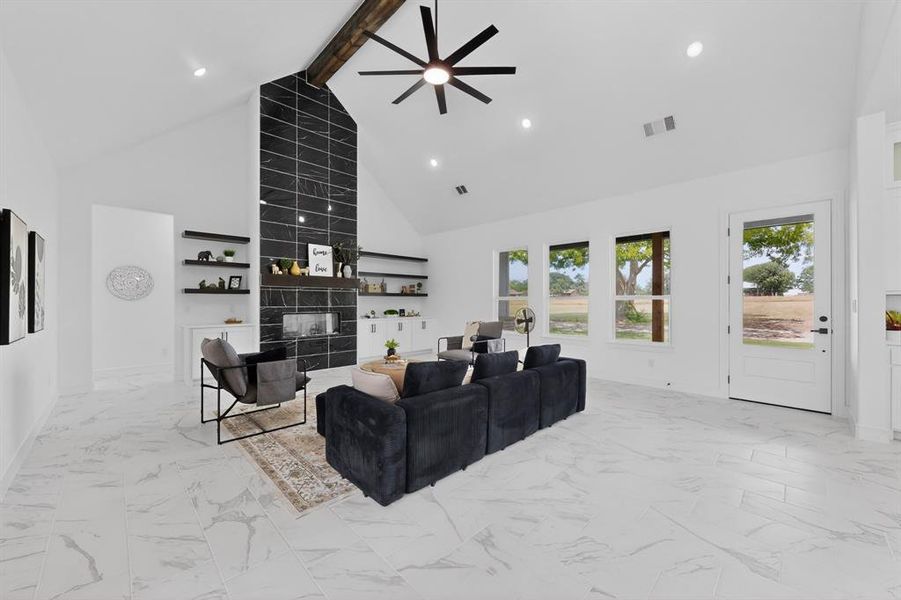 Spacious living area featuring a vaulted ceiling with exposed wood beam, a floor-to-ceiling tiled fireplace, recessed lighting, and large windows