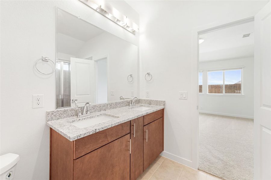 Bathroom with double sink vanity, wood cabinets, granite countertop, and large mirror above