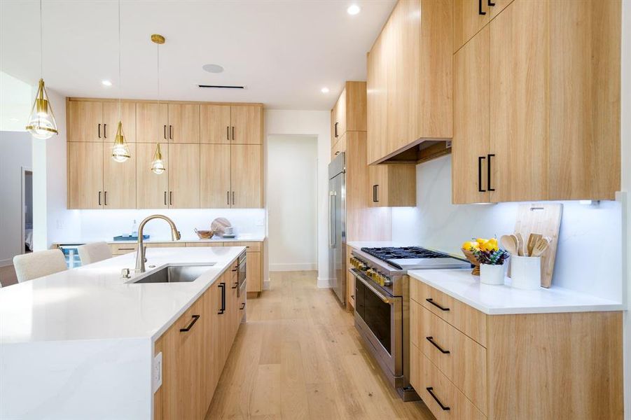 Kitchen with sink, light wood-type flooring, high end appliances, light brown cabinetry, and pendant lighting