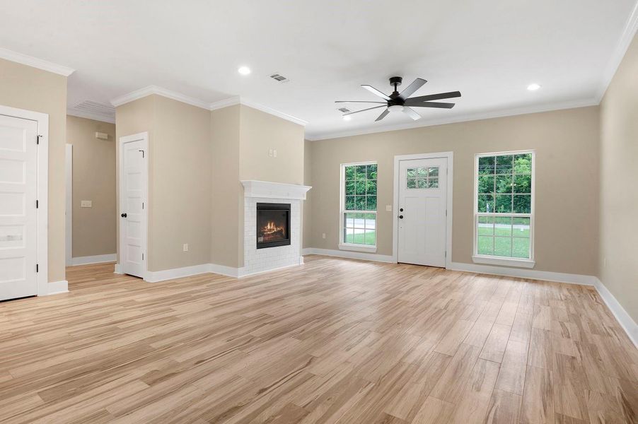 This spacious living room features elegant wood flooring, a cozy white brick fireplace, and ample natural light from large windows. A modern ceiling fan adds comfort, and the neutral walls create a warm, inviting atmosphere. This spacious living room features elegant wood flooring, a cozy white brick fireplace, and ample natural light from large windows. A modern ceiling fan adds comfort, and the neutral walls create a warm, inviting atmosphere.