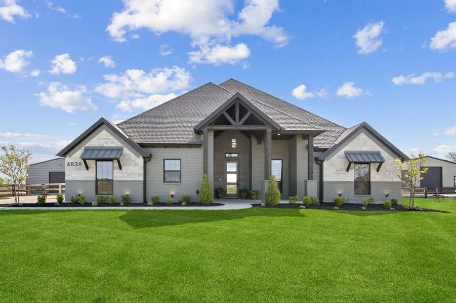 View of front facade with a shingled roof, brick siding, and stone siding