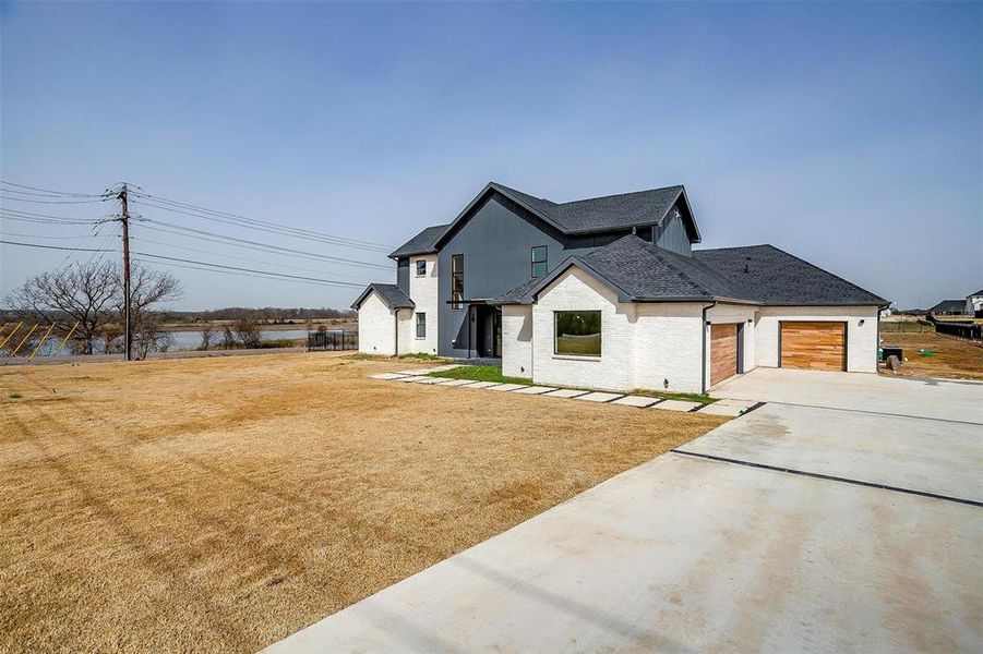 Modern farmhouse style home with an attached garage, brick siding, concrete driveway, roof with shingles, and a front lawn