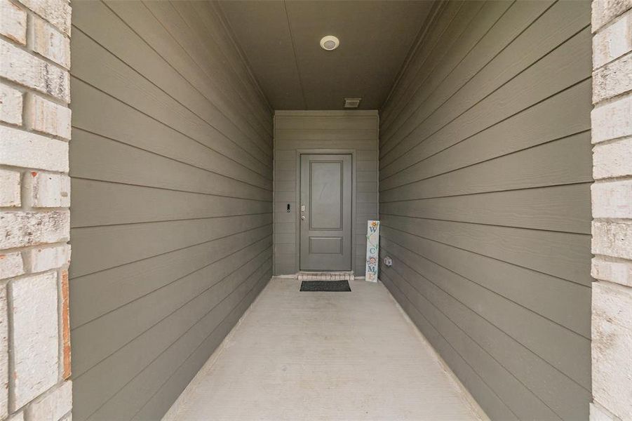 Covered entryway featuring a paneled door, horizontal siding, brick exterior accents, recessed lighting, and a concrete pathway