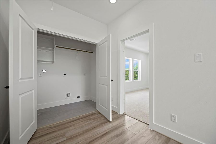 The modern laundry area with double doors, shelving, and space for appliances is located on the 3rd level. It leads into the primary bedroom with carpeted flooring and large windows, allowing plenty of natural light. The area has a clean, fresh look with neutral tones.