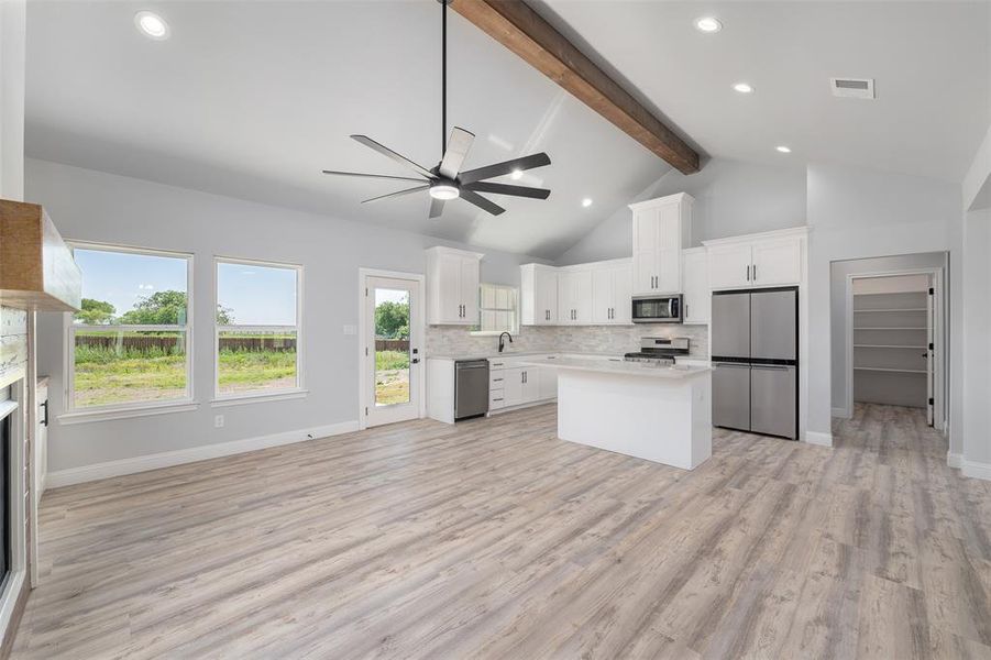 Kitchen featuring stainless steel appliances, light countertops, a sink, beam ceiling, and ceiling fan