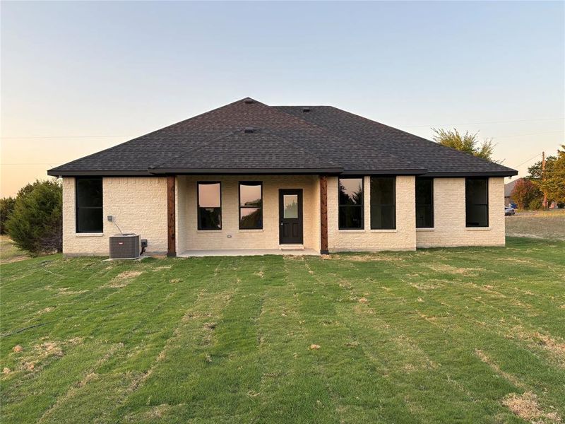 Back house at dusk featuring a patio area, central air condition unit, and a lawn