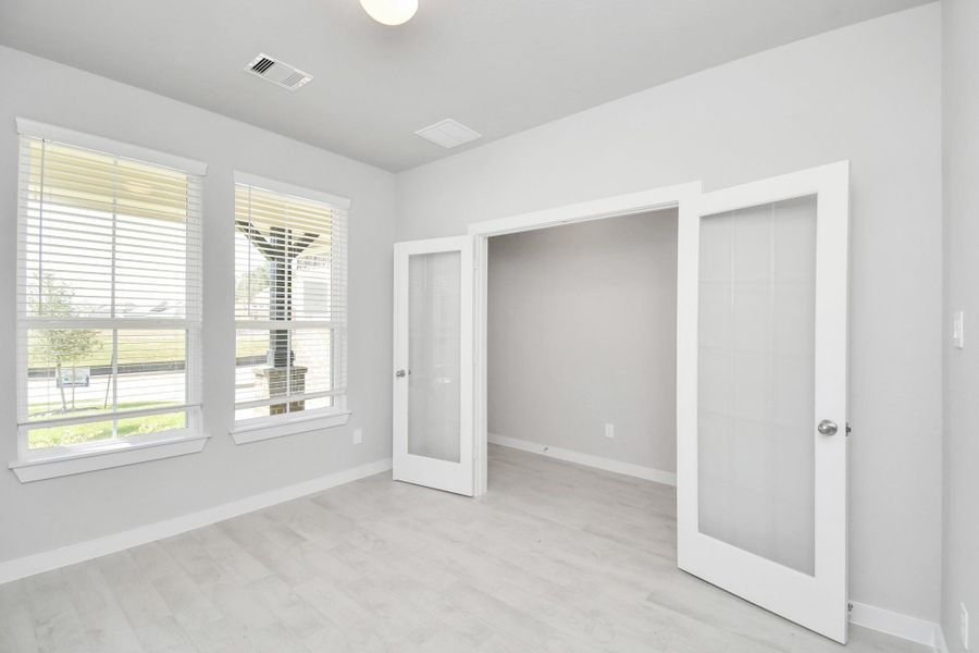 Experience the perfect blend of sophistication and warmth in this home office, boasting elegant wood-look tile flooring and flooded with natural light from expansive windows and French doors. Sample photo of completed home with similar floor plan. Actual colors and selections may vary.