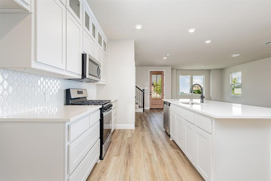 Kitchen with appliances with stainless steel finishes, white cabinetry, tasteful backsplash, light wood-style flooring, and recessed lighting