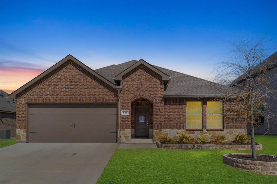 View of front of home featuring an attached garage, brick siding, concrete driveway, a yard, and roof with shingles