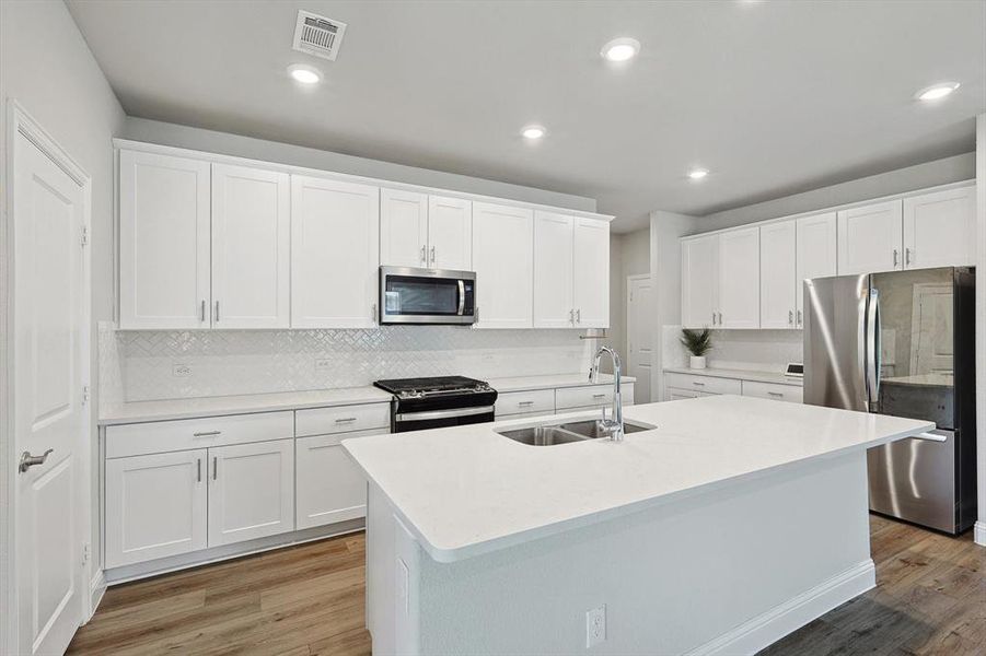 Kitchen with tasteful backsplash, stainless steel appliances, wood-type flooring, sink, and white cabinets